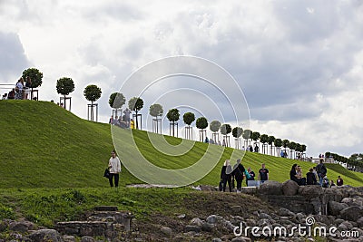 Row of manicured Tilia trees in line on and people walking on green grass lawn hill of Garden of Venus with blue sky Editorial Stock Photo