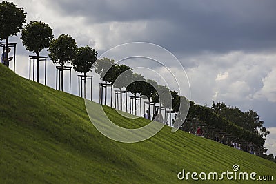 Row of manicured Tilia trees in line on and people walking on green grass lawn hill of Garden of Venus with blue sky Editorial Stock Photo