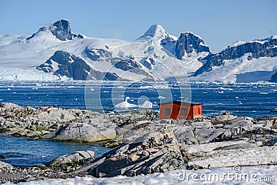 Petermann Island, beautiful Antarctic Island with penguins on rocks, abandoned station and snow covered mountains behind Ocean. Stock Photo