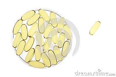 Petri dish of gold gel capsules with one apart Stock Photo