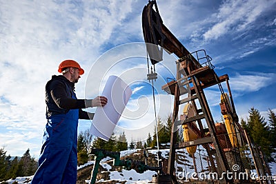 Oil worker standing in the oilfield next to a pump jack with a big paper Stock Photo