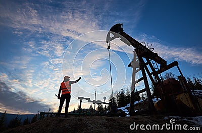 Petroleum operator pointing at oil well pump jack. Stock Photo