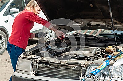 A young woman at the open bonnet of a car is trying to fix the malfunction Editorial Stock Photo