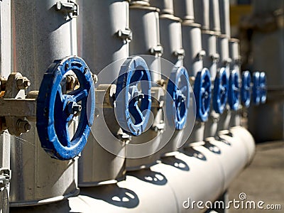 Phantom Blue industrial valves in a row on petrochemical plant pipelines system selective focus over out of focus background Stock Photo