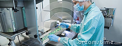 Pharmaceutical industry man worker in protective clothing operating production of tablets in sterile working conditions Stock Photo