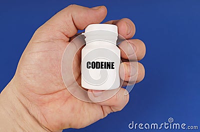 On a blue background in the hands of a man is a white jar with the inscription - Codeine Stock Photo