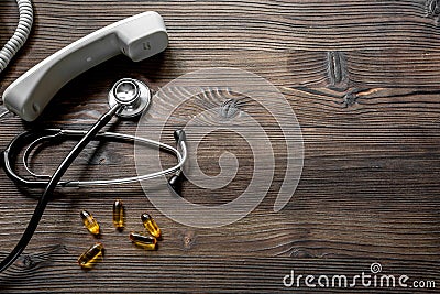 Phone handset, pills and phonendoscope on dark wooden desk top view make appointment with a doctor space for text Stock Photo