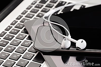 Phone and tablet with white headphones on laptop keyboard Stock Photo