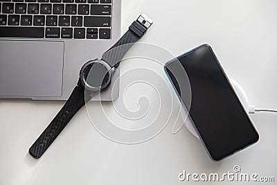 phone on wireless charger smart watch on laptop Editorial Stock Photo