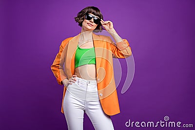 Photo of adorable shiny young woman dressed orange blazer arm dark glasses empty space smiling isolated purple color Stock Photo