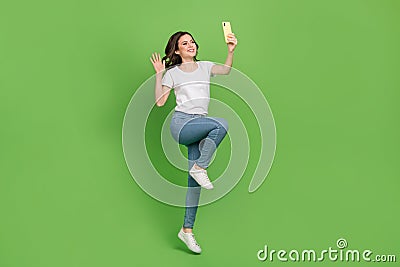 Photo of adorable sweet young lady wear white t-shirt jumping high video talk modern device isolated green color Stock Photo