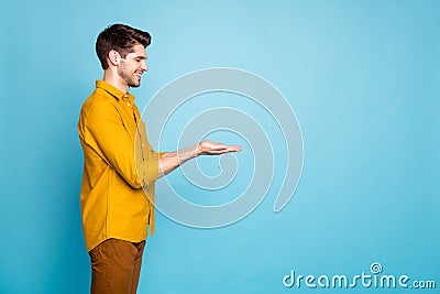 Photo of adoring man holding object with hands wearing yellow shirt trousers pants smiling toothily with eyes closed Stock Photo
