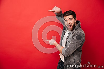 Photo of agitated man wih beard in casual clothing pointing fingers on copyspace text or product with surprise and smile, isolate Stock Photo