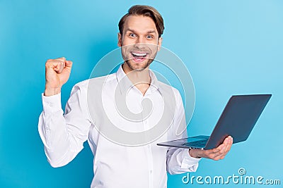 Photo of amazed happy victorious young man raise fist hold laptop winner isolated on blue color background Stock Photo