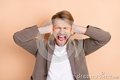 Photo of annoyed unhappy young guy wear jacket shouting arms cover ears isolated beige color background Stock Photo