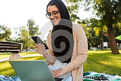 Photo of attractive arabic woman wearing headscarf using silver laptop Stock Photo