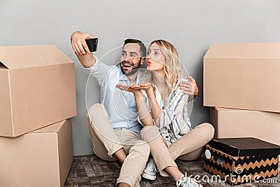 Photo of attractive couple seating near cardboard boxes and taking selfie photo on cellphone Stock Photo