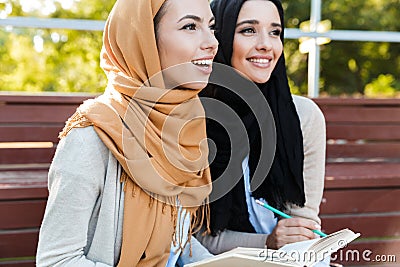 Photo of attractive muslim girls wearing headscarfs sitting in green park Stock Photo
