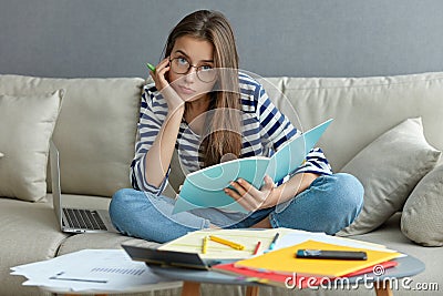 Photo of attractive woman writes article, develops startup project, enjoys comfort, poses in living room on sofa with Stock Photo