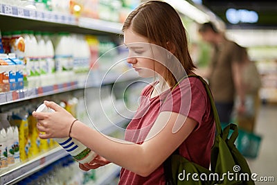 Photo of attractive young female consumer model with bobbed hairstyle, dressed in casual t shirt, stands in big store, holds bottl Stock Photo