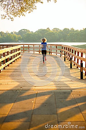 Photo from back of sports woman running on wooden bridge on summer. Stock Photo