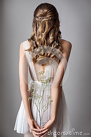 Photo from the back of a very beautiful young model in white dress with gypsophila flowers in her hands. Romantic style. Stock Photo