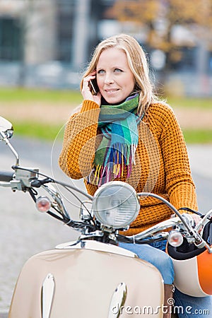 Portrait of beautiful woman talking on smartphone while waiting and sitting on motorbike in park Stock Photo