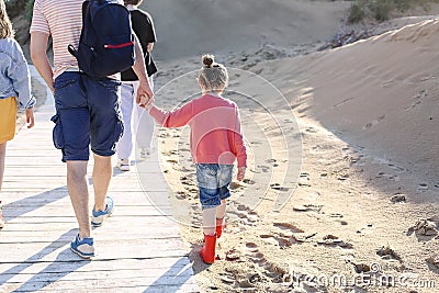 Photo from behind of happy family walking on wooden path on sunny sand beach Stock Photo