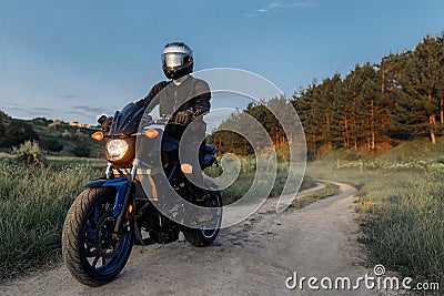 Photo of biker driving motorcycle in sunset on the country road. Stock Photo