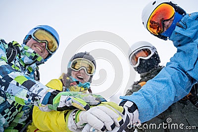 Photo from bottom of four happy snowboarders in helmet doing handshake on blue sky. Stock Photo