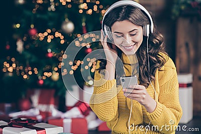 Photo of charming beautiful wavy curly haired girl listening to music wearing yellow pullover staring at telephone Stock Photo