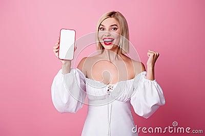 Photo of charming lucky lady wear off shoulders dress rising fist modern gadget display empty space isolated pink color Stock Photo