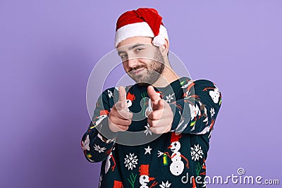 Photo of cheerful bearded man wearing santa hat and funny sweater with snowmen, handsome guy posing isolated over lilac studio Stock Photo