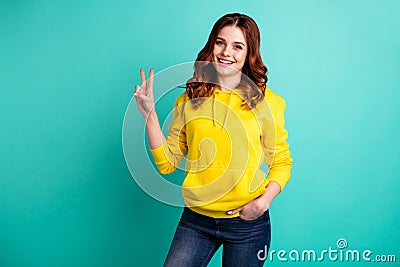 Photo of cheerful charming positive cute nice youngster holding hand in denim pockets showing you v-sign isolated over Stock Photo