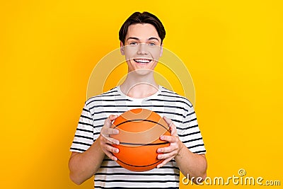 Photo of cheerful positive student with stylish hairdo dressed striped t-shirt hold bascketball ball isolated on yellow Stock Photo