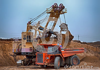 Photo of the coal mine. Autotruck under loading: the excavator loads overburden rock into it. Stock Photo