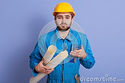 Photo of confused indignated young engineer having helpless facial expression, explaining, making gesture, wearing yellow helmet Stock Photo