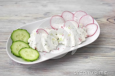 A photo of cottage cheese decorated with radish and cucumbe on the white plate. Curd sandwiches and herbs. Organic rustic food. Stock Photo