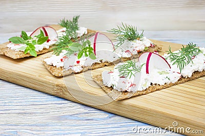 A photo of crackers, crisp rye bread toast with cottage cheese decorated with radish, cucumber, dill and basil leaves the wooden b Stock Photo