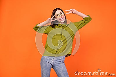 Photo of crazy brunette hairdo young lady show v-sign wear specatcles green shirt isolated on orange color background Stock Photo