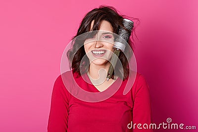 Photo of dark haired girl combs her hair, has some problems, hairbrush tangled in curls, stands smiling against rose wall, wears Stock Photo
