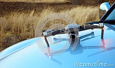 Photo of a drone with its reflection on the hood of a car and yellow autumn grass in the background Stock Photo