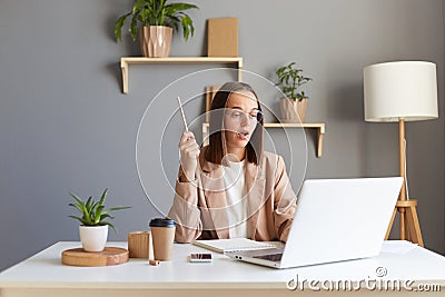 Photo of excited amazed inspired Caucasian woman wearing beige jacket posing in office, raised her hand and keeps mouth open, Stock Photo