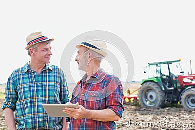 Farmers using digital tablet while standing against tractor in field Stock Photo
