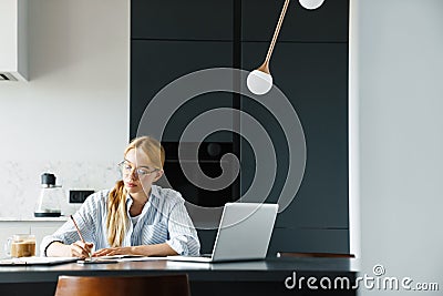 Photo of focused woman making down notes while working with laptop Stock Photo