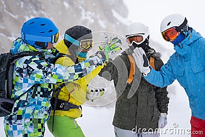 Photo of four happy snowboarders in helmet doing handshake on mountains background . Stock Photo