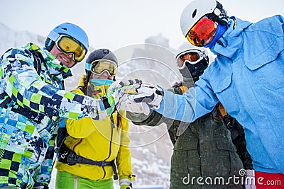 Photo of four happy snowboarders in helmet doing handshake at snow resort. Stock Photo