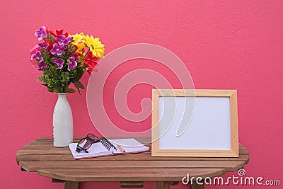 Photo Frame on a wooden table and book and Flowers in jar on pink background . Stock Photo