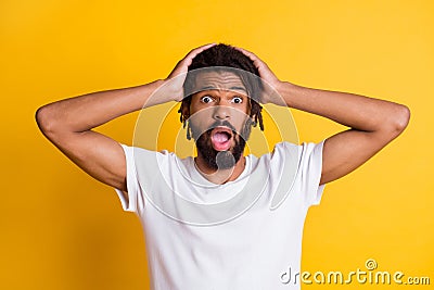 Photo of frightened dark skin guy open mouth awful news arms on head wear t-shirt isolated yellow color background Stock Photo