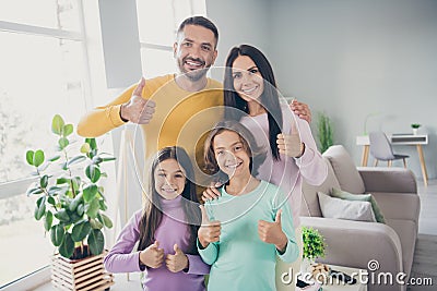 Photo of full family four members two little kids raise thumb up toothy beaming smile wear colorful pullover in living Stock Photo